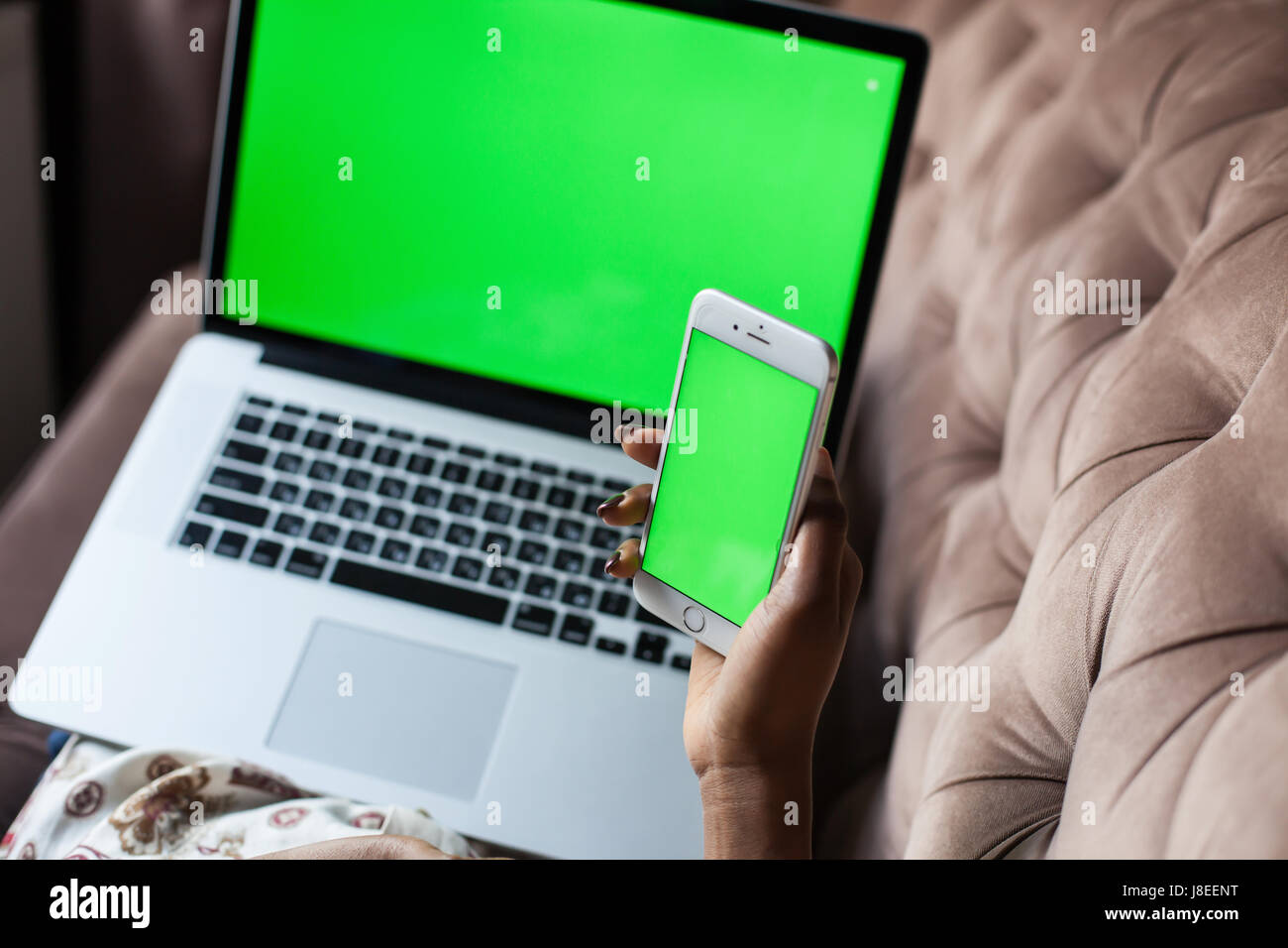 Close up shot of woman's hands holding phone and laptop with green screens. Stock Photo