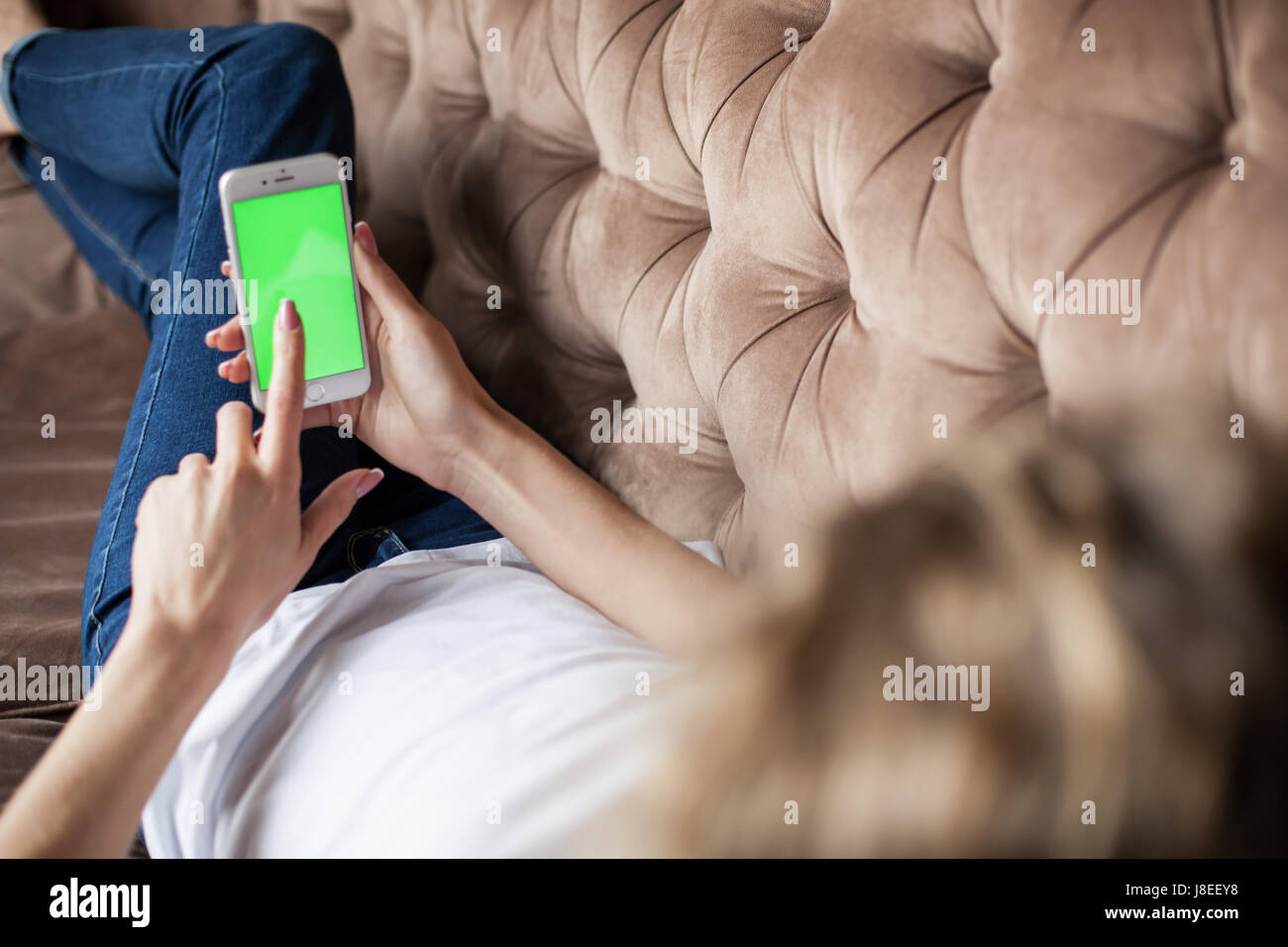 Beautiful girl lying on the sofa with the phone in her hands. Phone with green screen. Stock Photo
