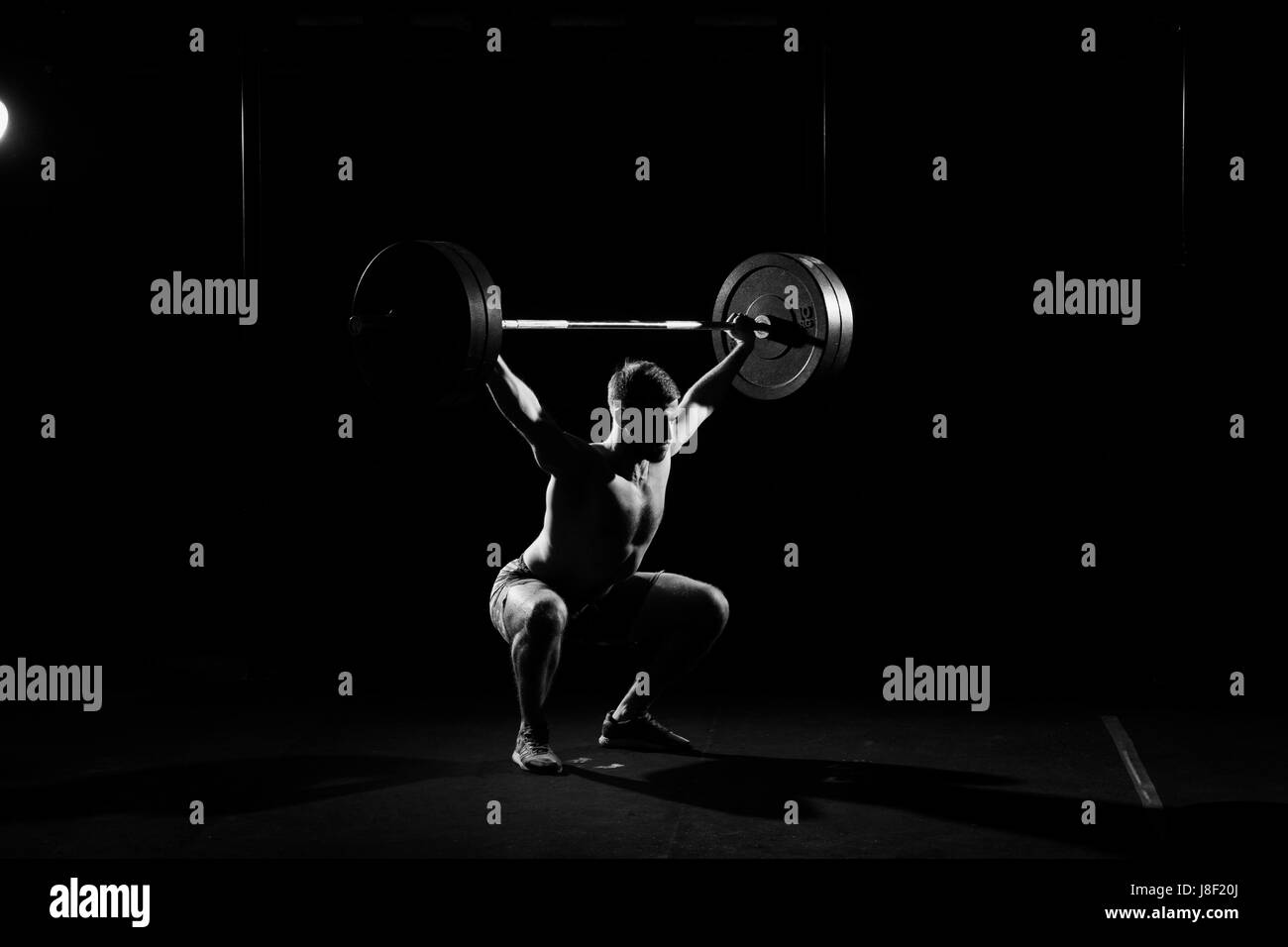 Fitness training. Man doing sit ups exercise with barbell in dark gym. Stock Photo