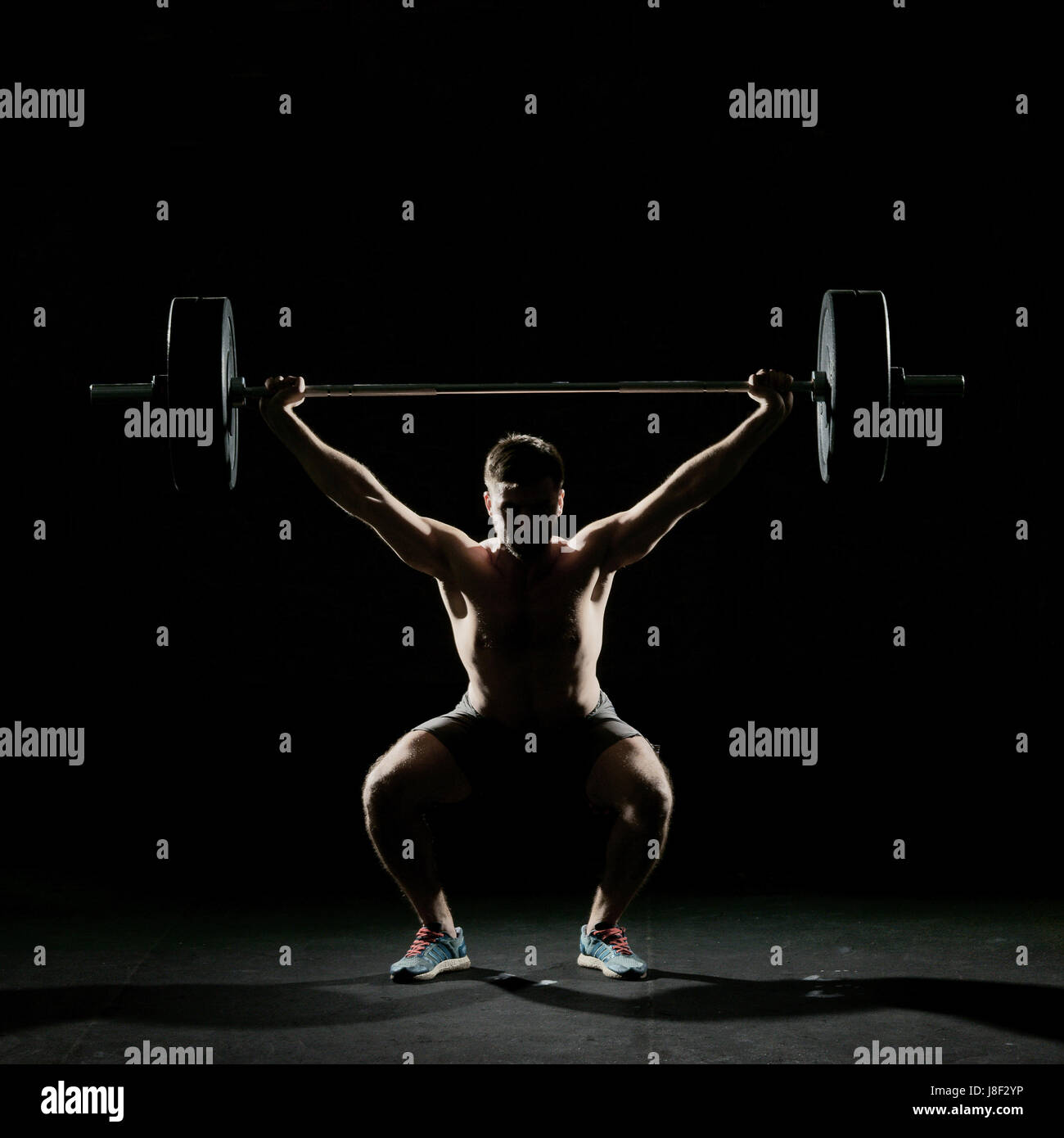 Fitness training. Man doing sit ups exercise with barbell in dark gym