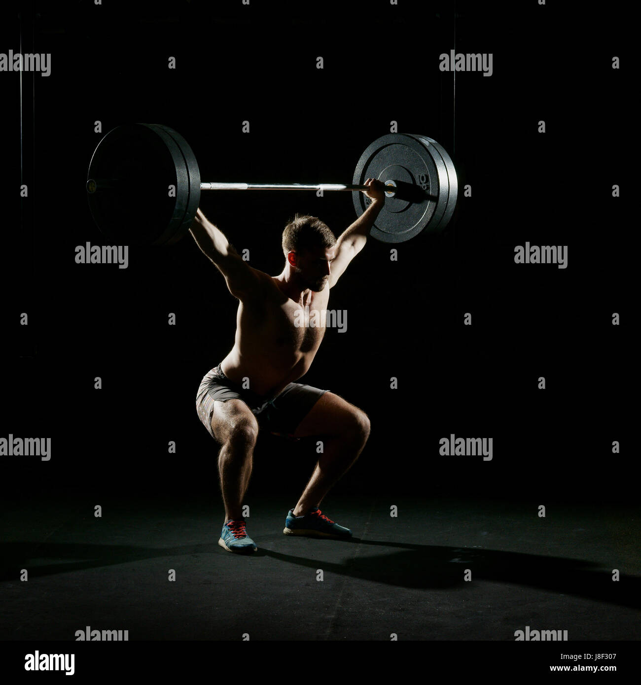 Fitness training. Man doing sit ups exercise with barbell in dark gym