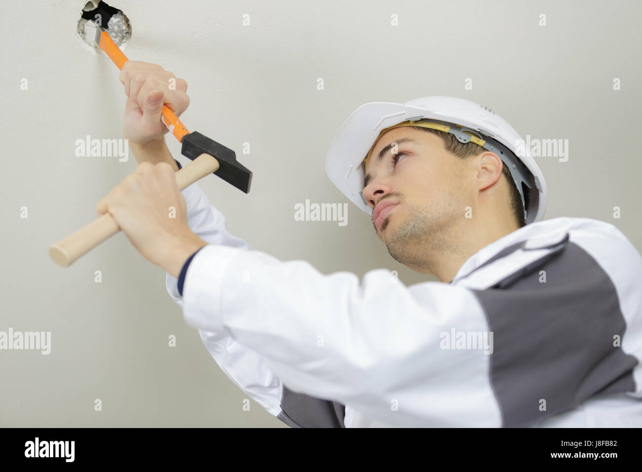 the worker scrapes the old paint on the ceiling Stock Photo