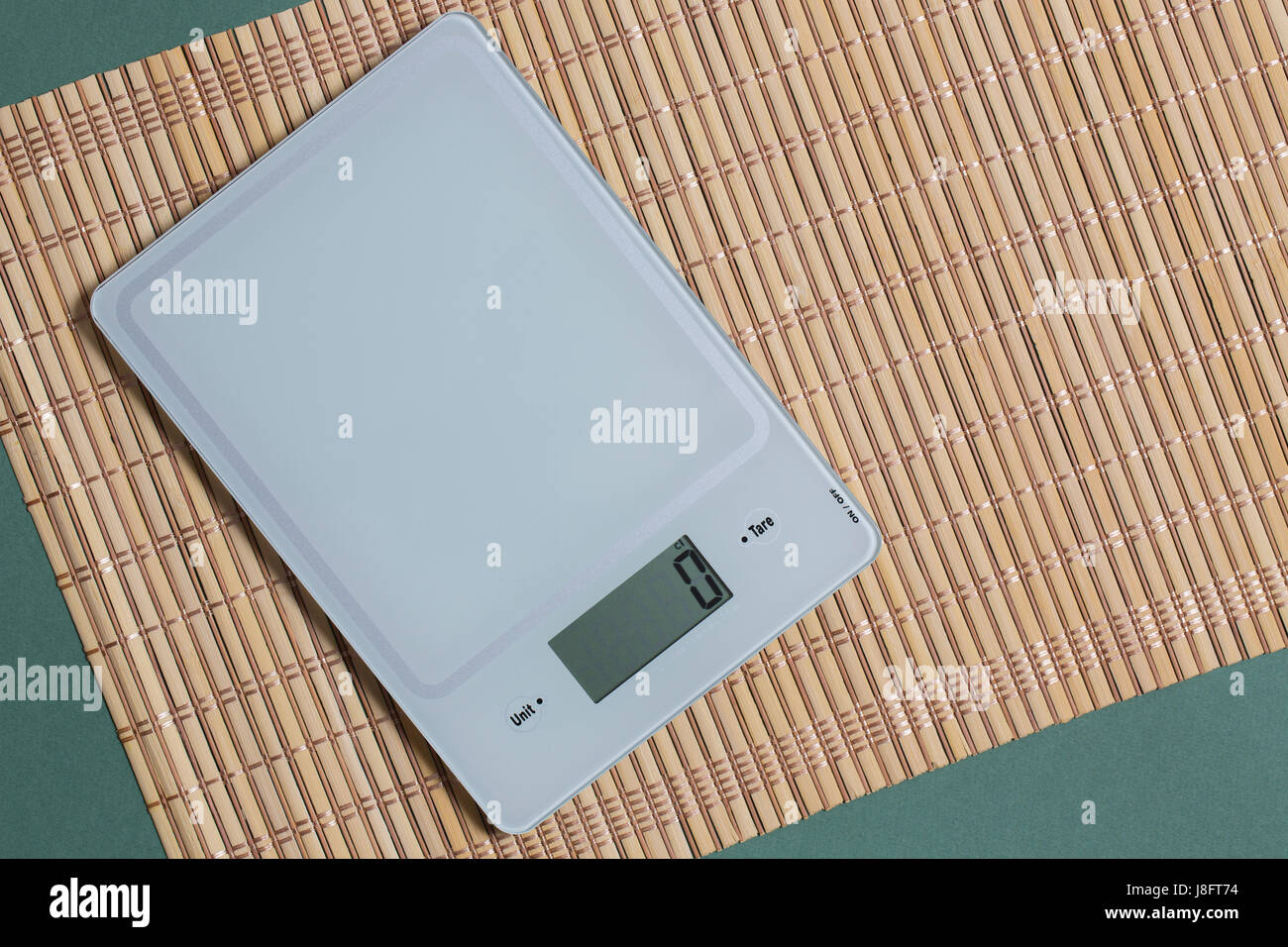 Empty kitchen scale on bamboo mat and green paper background. Stock Photo