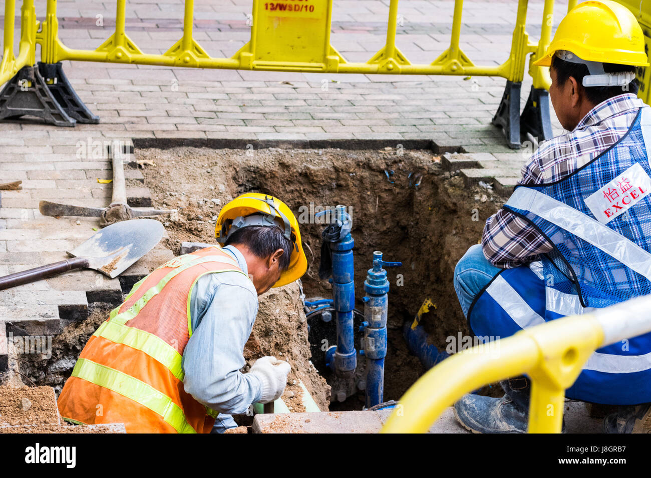 Workers digging a hole in sidewalk for repairs or maintenance Stock Photo
