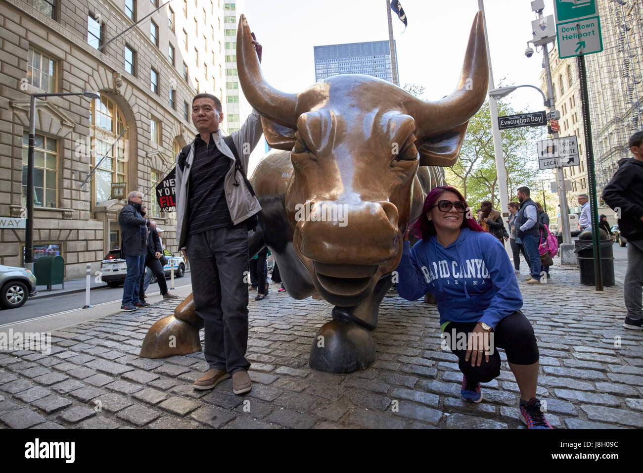 tourists pose for photos at charging bull sculpture New York City public art bowling green broadway USA Stock Photo