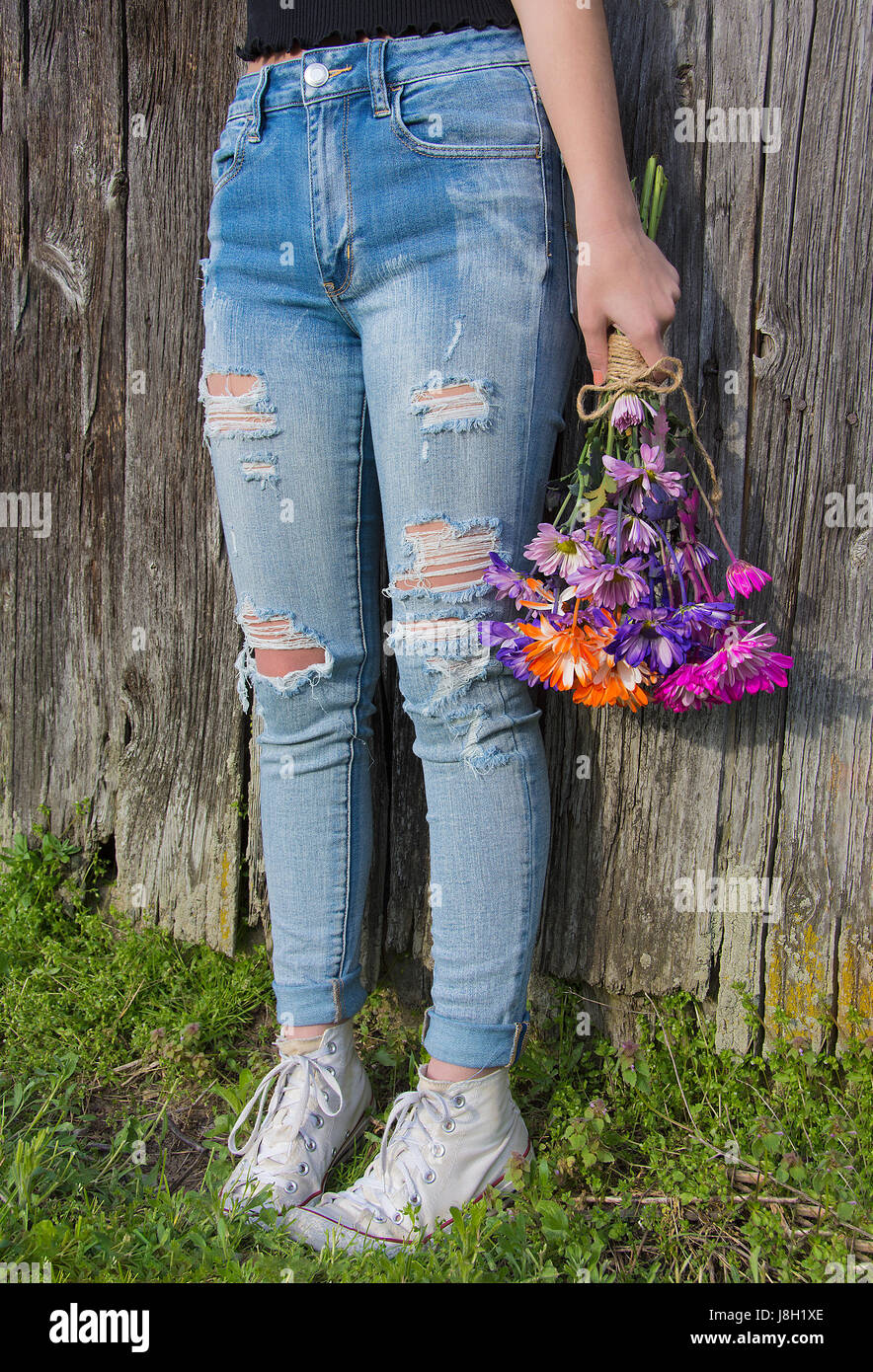 teenage girl wearing sneakers and frayed blue jeans with colorful daisy  bouquet by old barn Stock Photo - Alamy