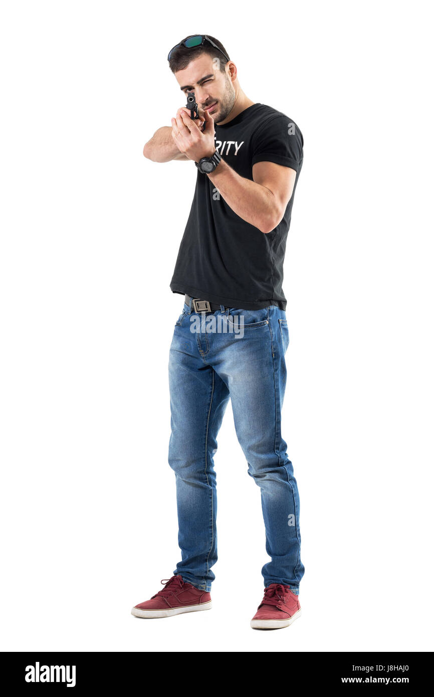 Plain clothes young policeman pointing gun with both hands aiming with one eye. Full body length portrait isolated on white studio background. Stock Photo