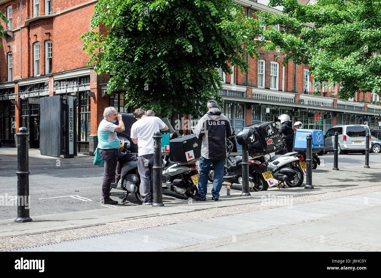 Deliveroo, Uber Eats and Stuart food delivery couriers chat while waiting for customer delivery requests. Stock Photo