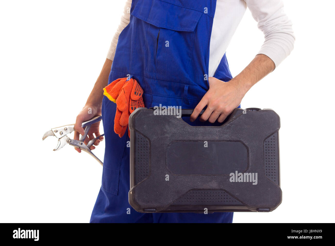 Young man in white shirt and blue overall with orange gloves holding spanner and black toolbox on white background in studio Stock Photo