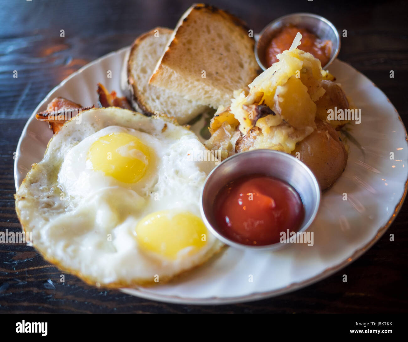 Two sunny side up eggs, hash brown potatoes, sourdough toast, and bacon (Canadian breakfast