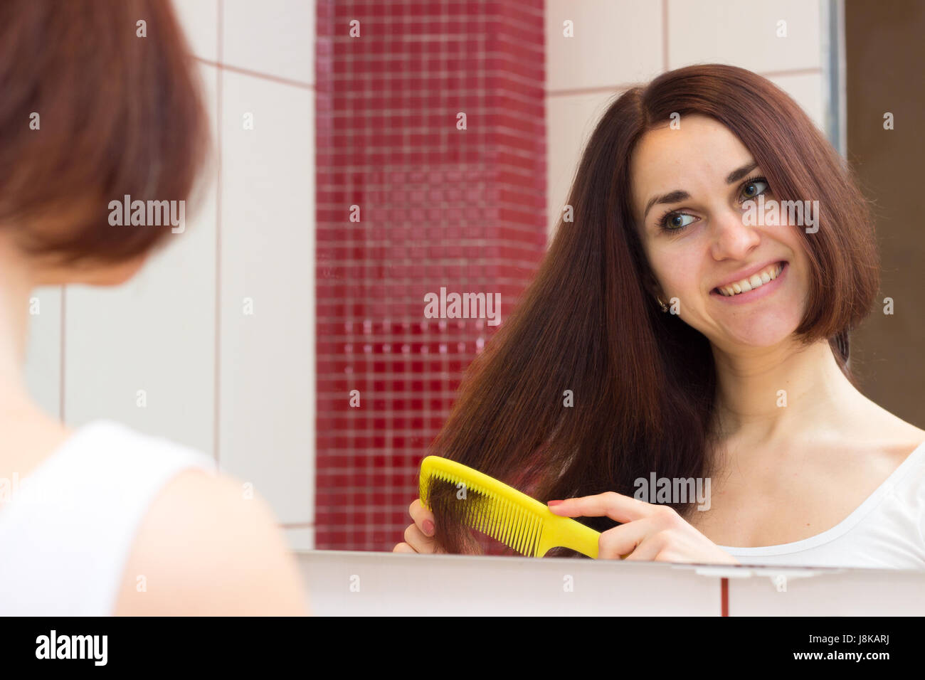 Young woman brushing her hair in bathroom Stock Photo