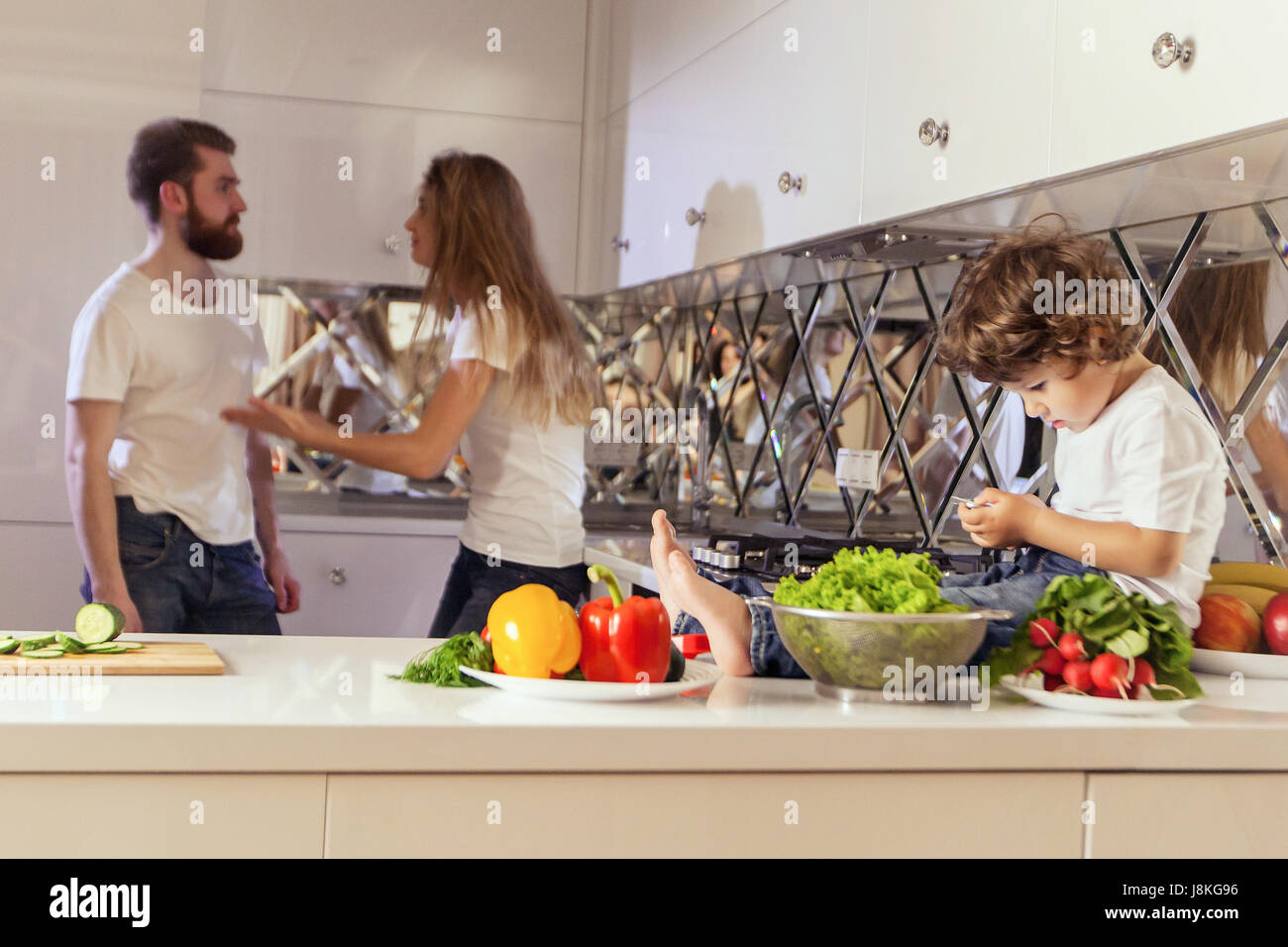 Little boy looking at the phone screen while his parents have conflict on the background. Stock Photo