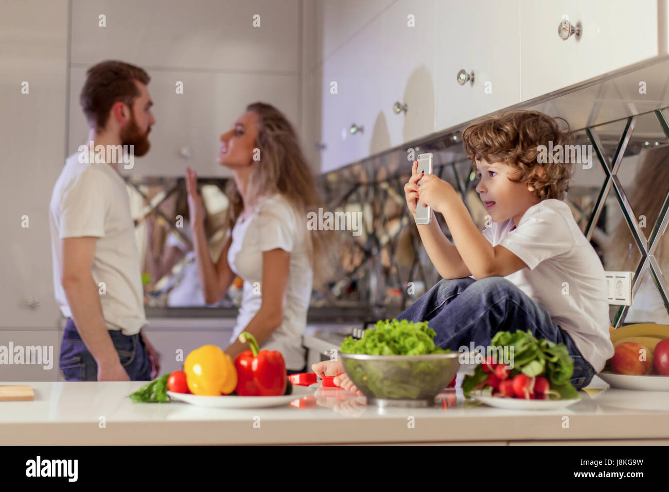 Family conflict photo. Small boy looking at the phone screen while parents have conflict. Stock Photo