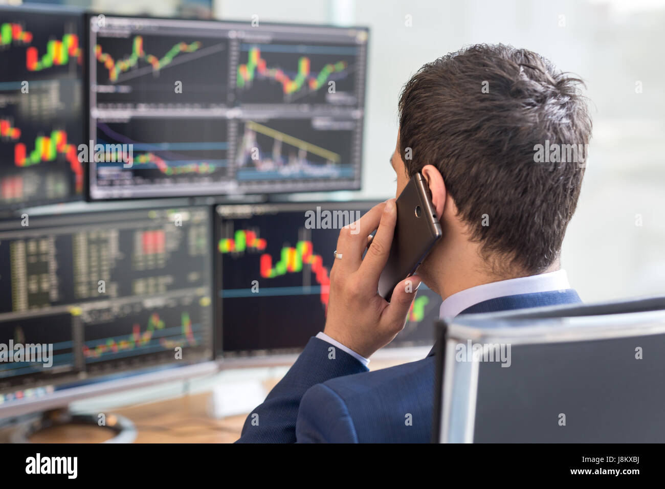 Over the shoulder view of stock broker trading online, talking on mobile phone. Stock Photo