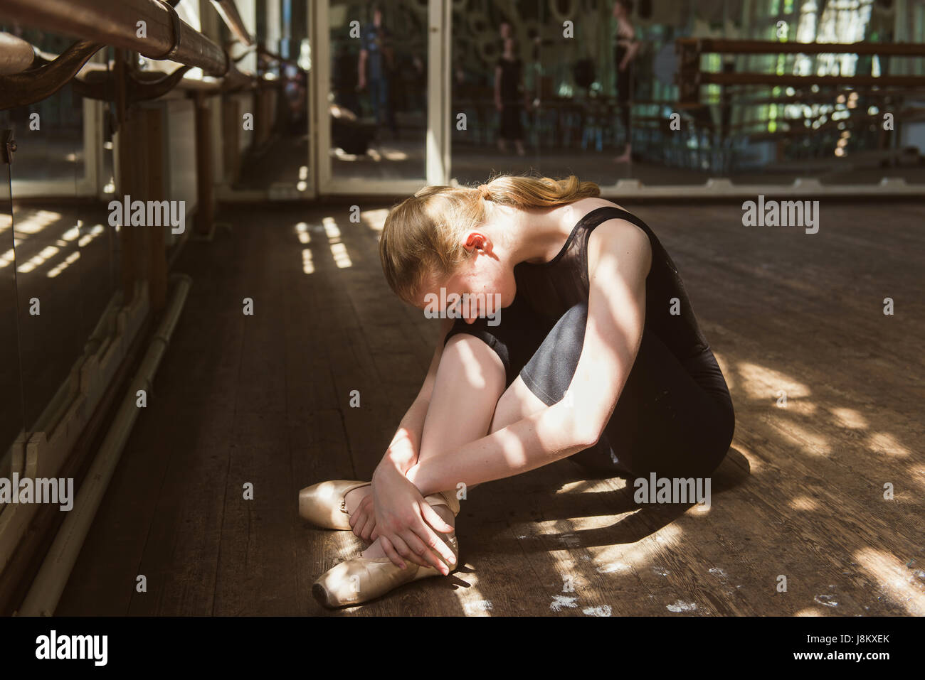Young ballet dancer practicing in class. Ballerina doing exercises. Girl stretches herself in the dancing hall. Stock Photo