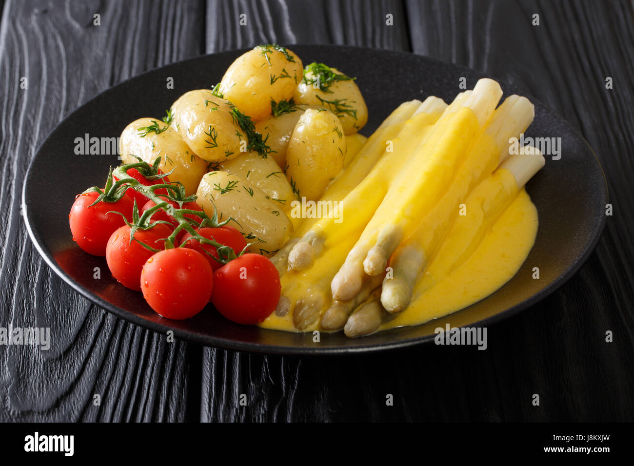 white asparagus with hollandaise sauce, new potatoes and tomatoes closeup on a plate