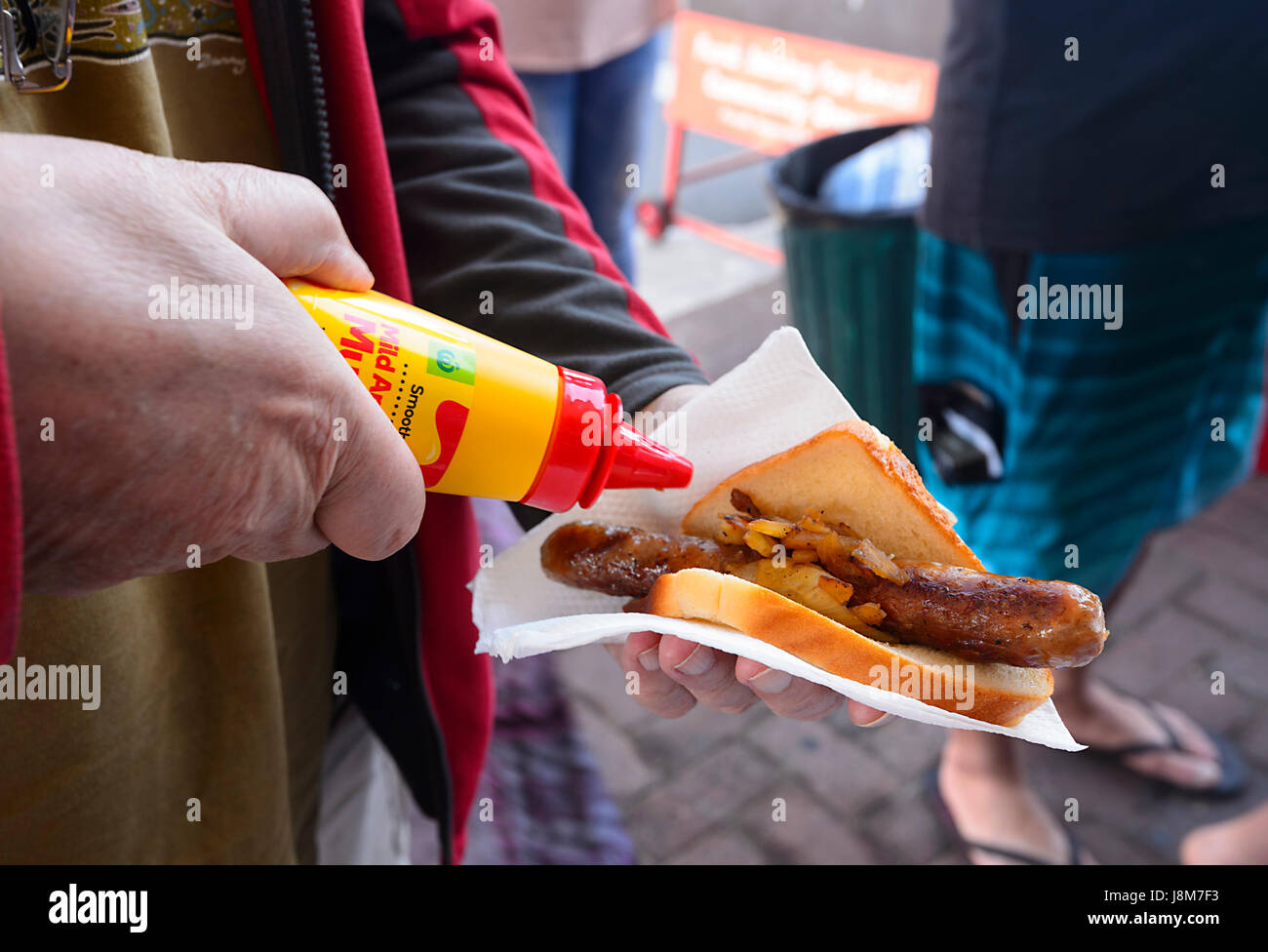 Person pouring mustard on a Bunnings Warehouse Sausage Sizzle done for Fund Raising, New South Wales, NSW, Australia Stock Photo