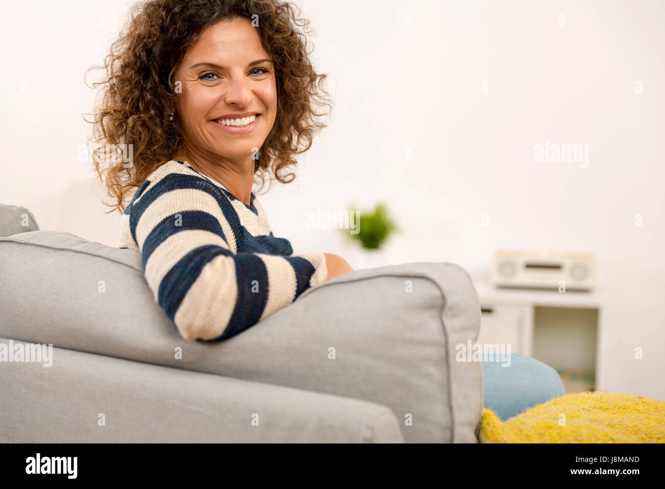 Beautiful woman sitting on the sofa and smiling Stock Photo - Alamy
