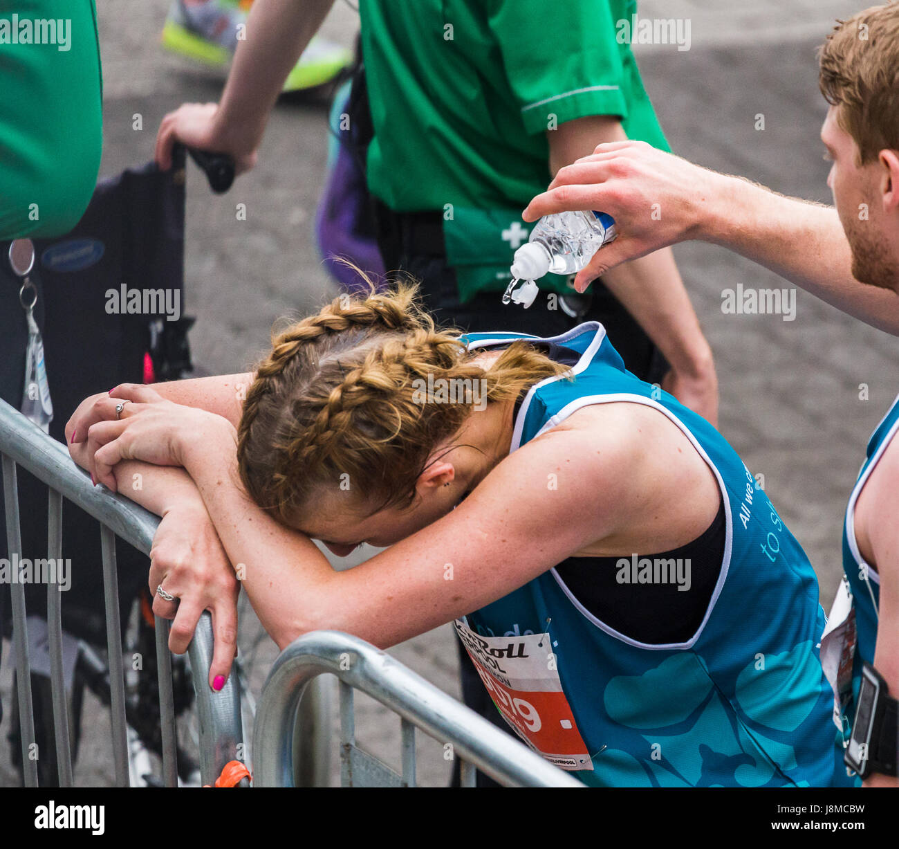 A man helps to cool off a young woman by splashing her with cold water at the end of the 2017 Liverpool Rock n Roll half marathon on 28 May 2017. Stock Photo