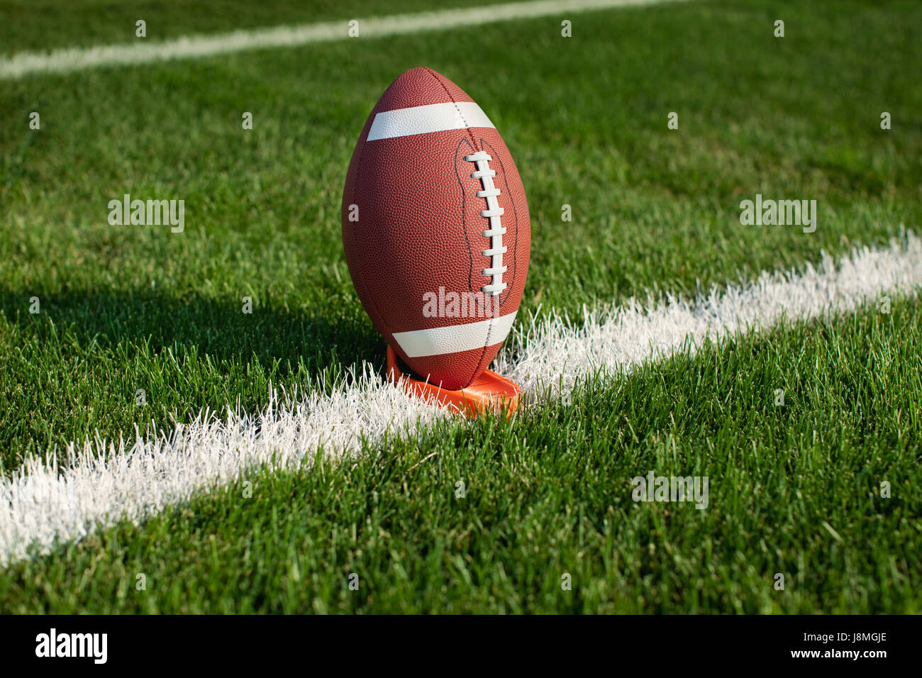 A college football sits on a tee at a yard line ready for kickoff Stock