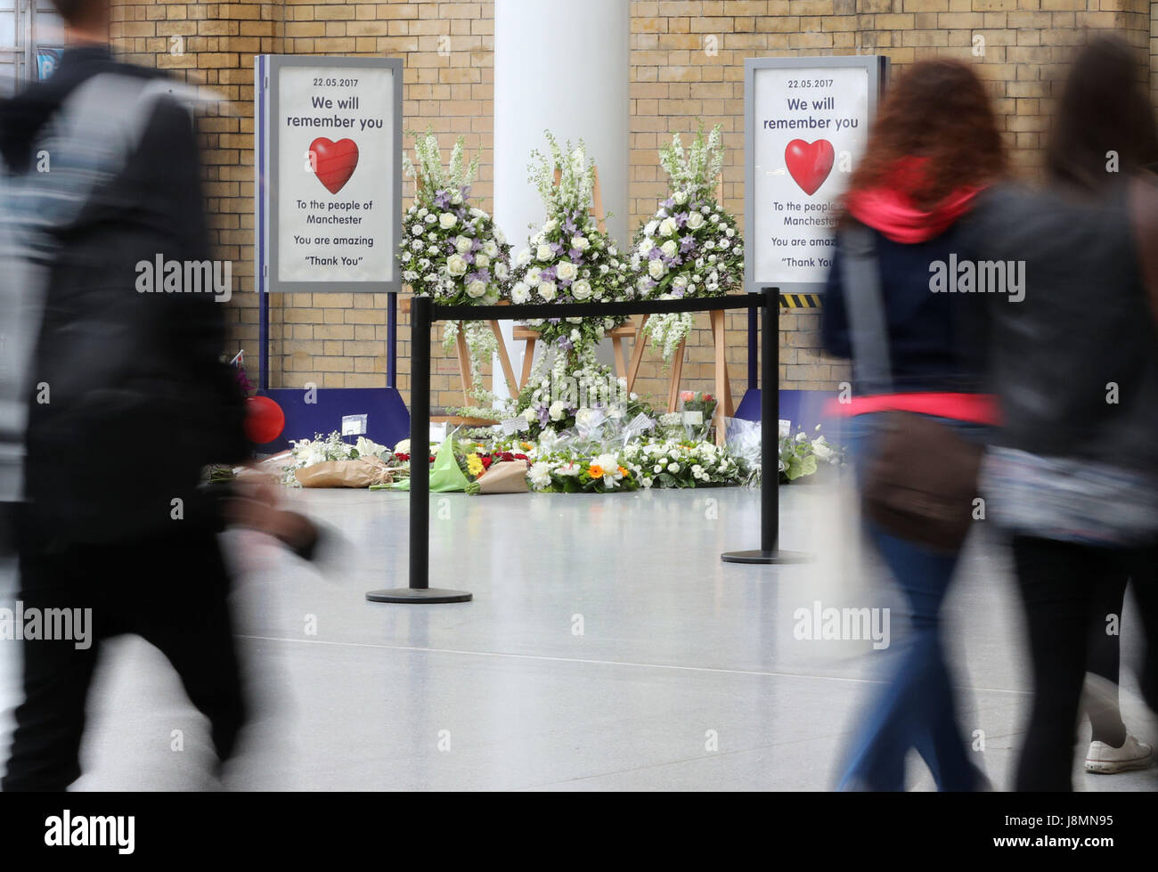 Commuters pass floral tributes at Manchester Victoria railway station which has reopened for the first time since the terror attack on the adjacent Manchester Arena. Stock Photo