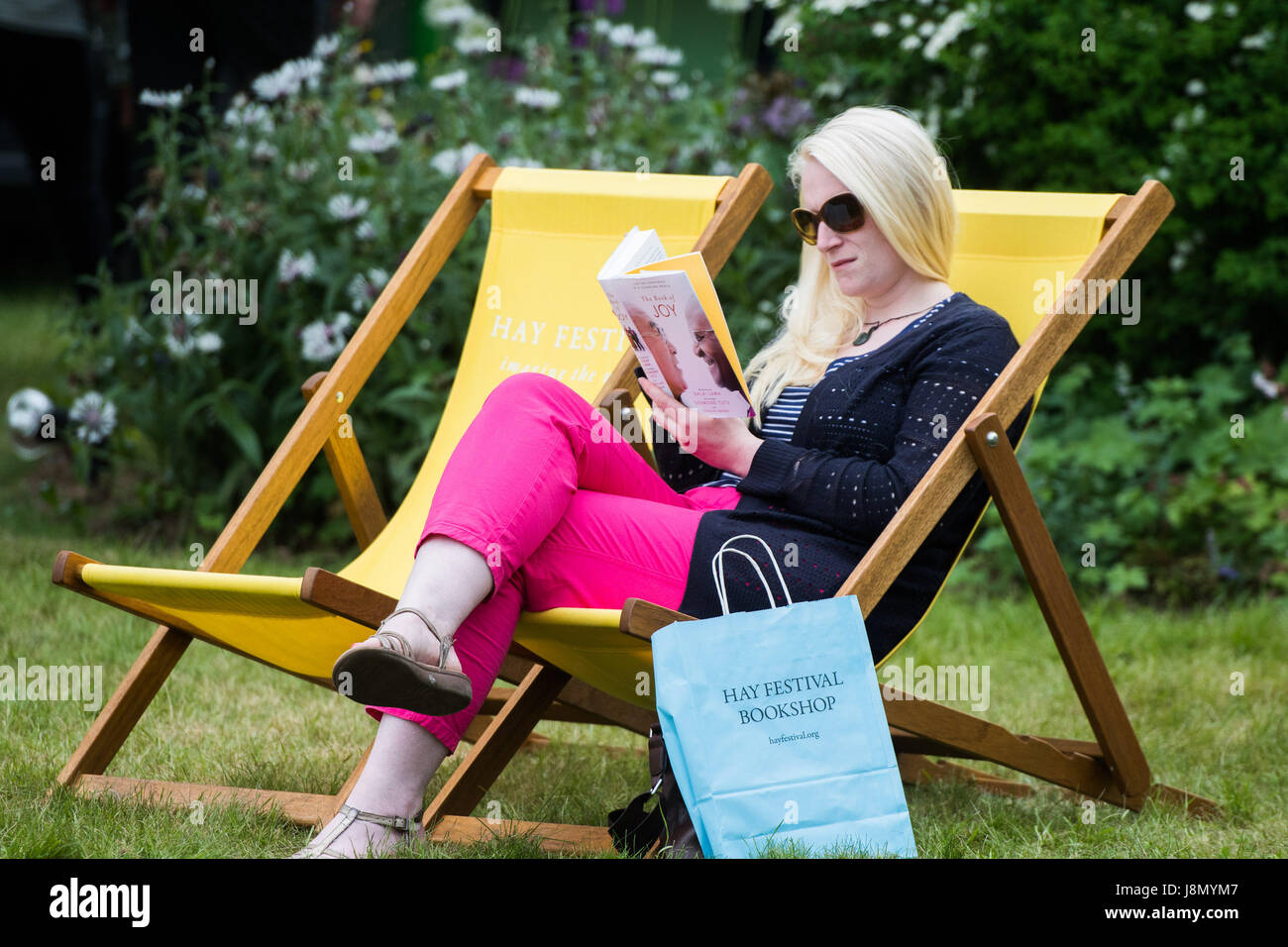 Hay Festival, Wales UK, Monday 29 May 2017 A woman reading and relaxing in the colourful deck-chairs on the lawn on a warm and muggy Bank Holiday Monday afternoon at the Hay Literature Festival 2017 Now in its 30th year, the festival draws tens of thousand of visitors a day to what was described by former US president Bill Clinton as "the woodstock of the mind" Photo credit Credit: keith morris/Alamy Live News Stock Photo