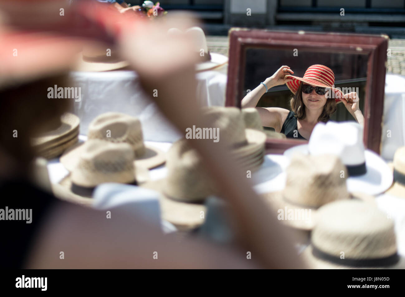Sarah tries on a straw hat at a stand selling headwear at the Muenster market in Freiburg, Germany, 29 May 2017. Photo: Patrick Seeger/dpa Stock Photo