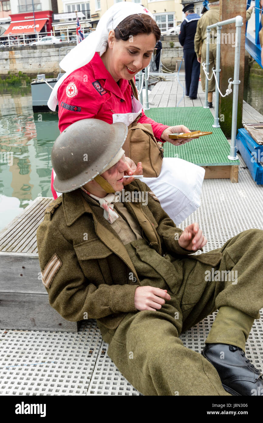 Dunkirk re-enactment at Ramsgate harbour, England. Red Cross nurse tending to wounded British soldier on deck of launch type boat, the P22 rhine river patrol boat. Soldier half laying on deck, smoking. Stock Photo