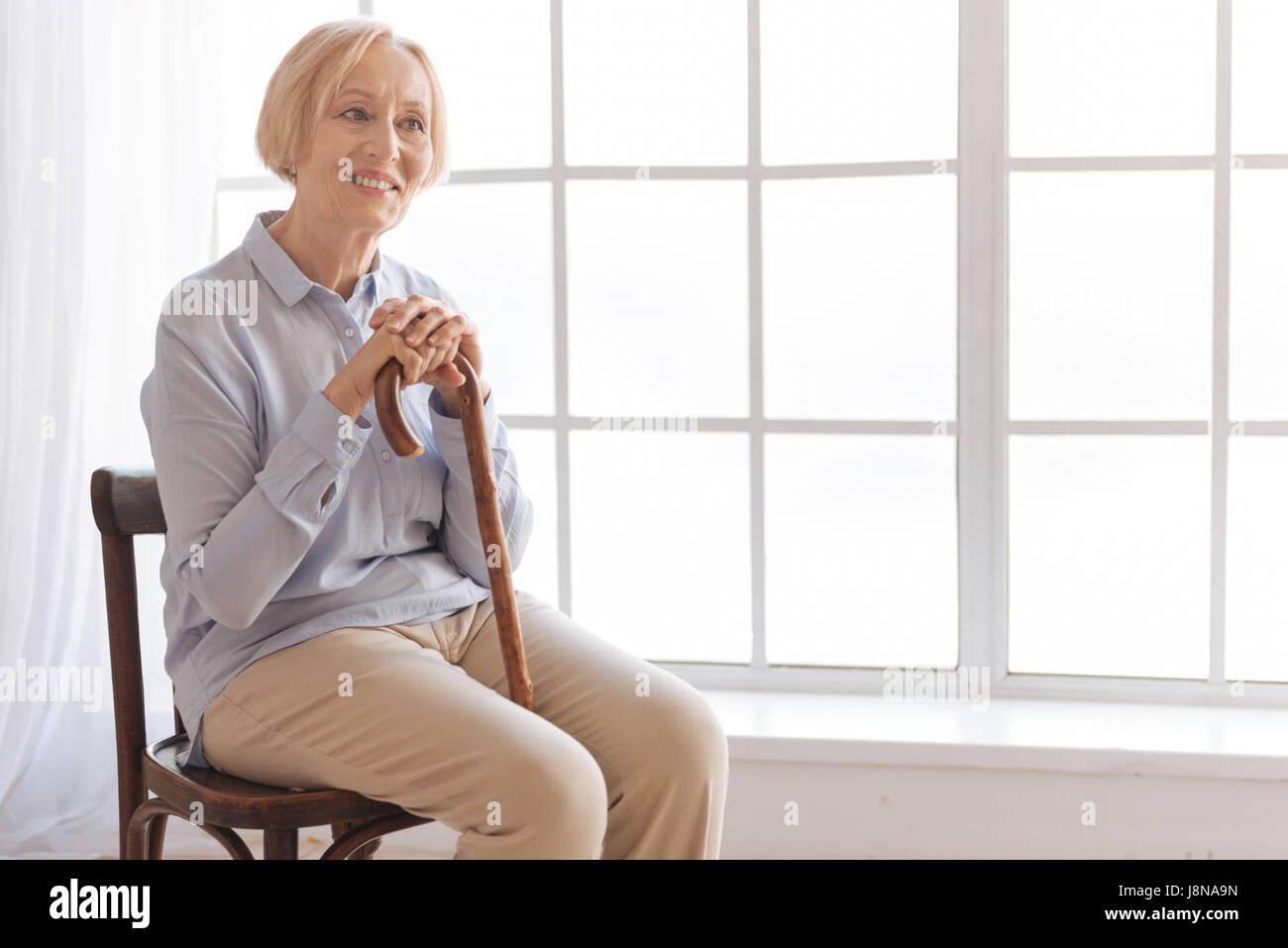 Keep your smile. Attractive woman putting hands on the cane sitting in ...