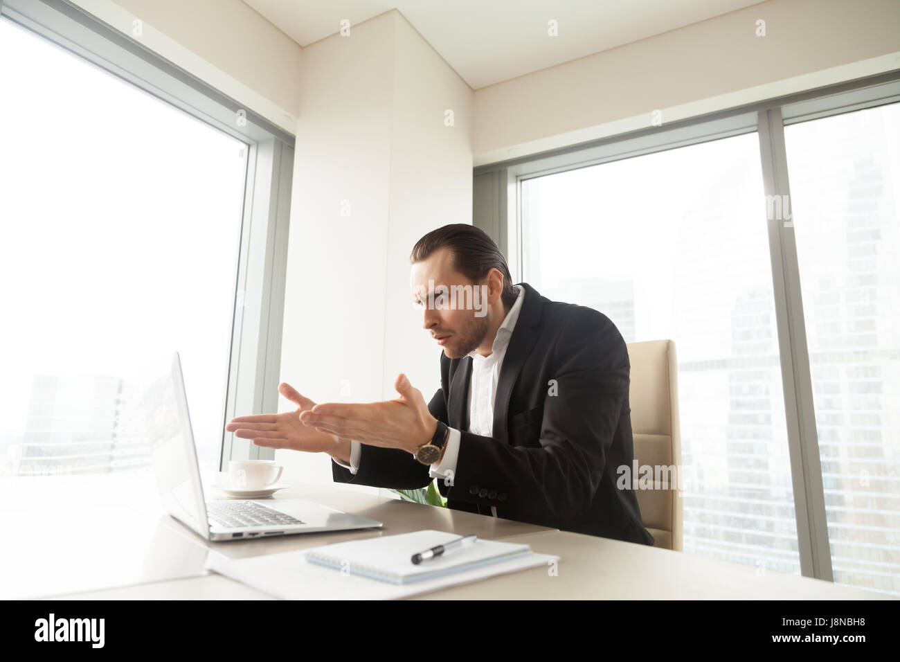 Shocked entrepreneur looking with surprise, pointing at computer on desk. Businessman upset because of unexpected data loss, wrong work result, bad jo Stock Photo