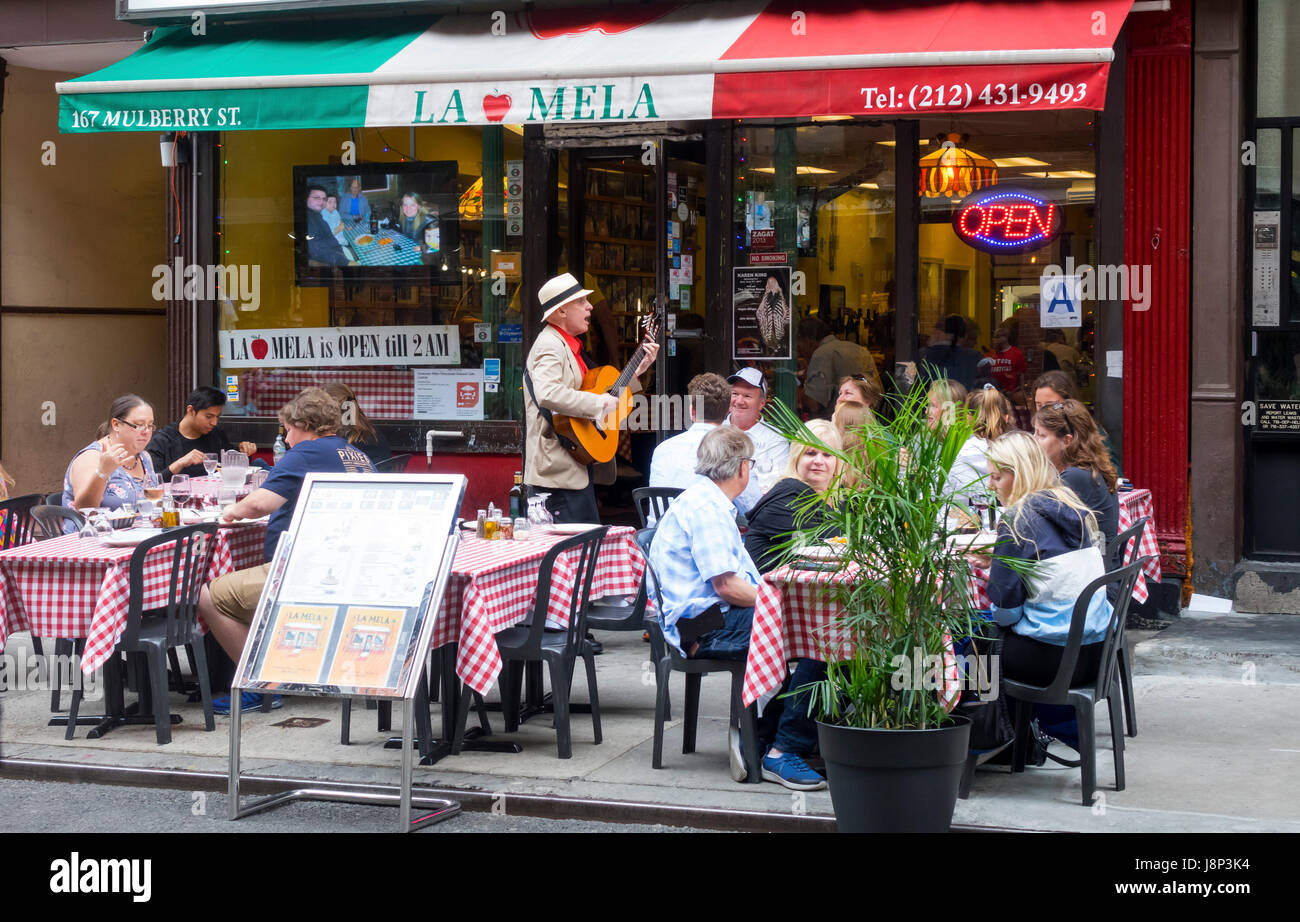 An Italian senior busker sings and plays for the alfresco dinners at La Mela, a restaurant on Mulberry Street in Little Italy, New York City Stock Photo