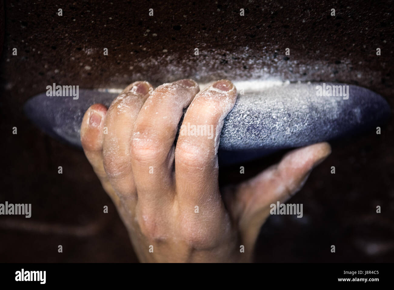 Woman's hand on handhold indoor climbing wall close up on chalk covered fingers Stock Photo