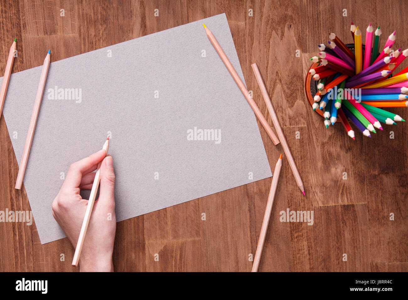 Girl hand drawing, blank grey paper and colorful pencils on wooden table Stock Photo