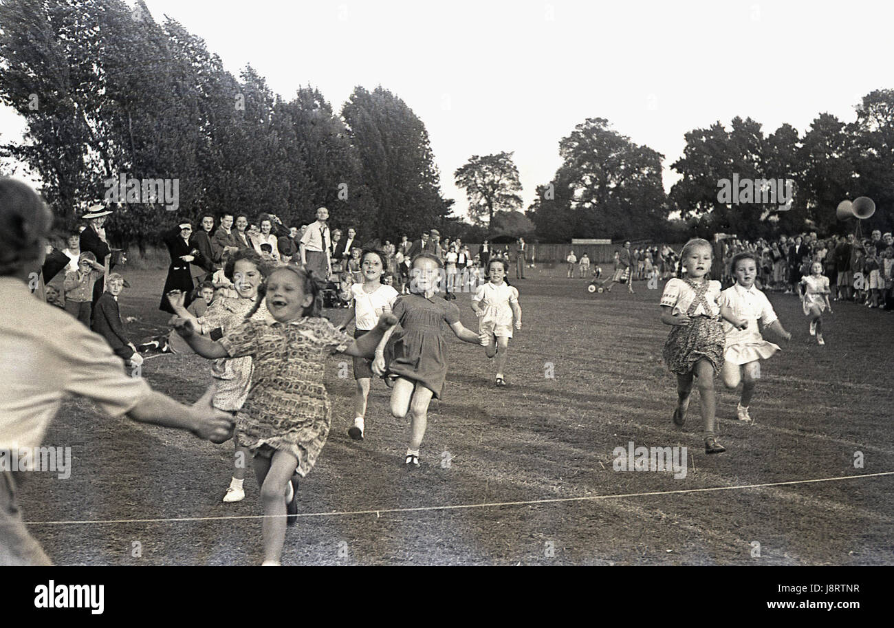 1950s. historical, young girls running in the 60 yard dash at a school sports day, with one joyful youngster about to win the race and into her mother's arms, England, UK. Stock Photo