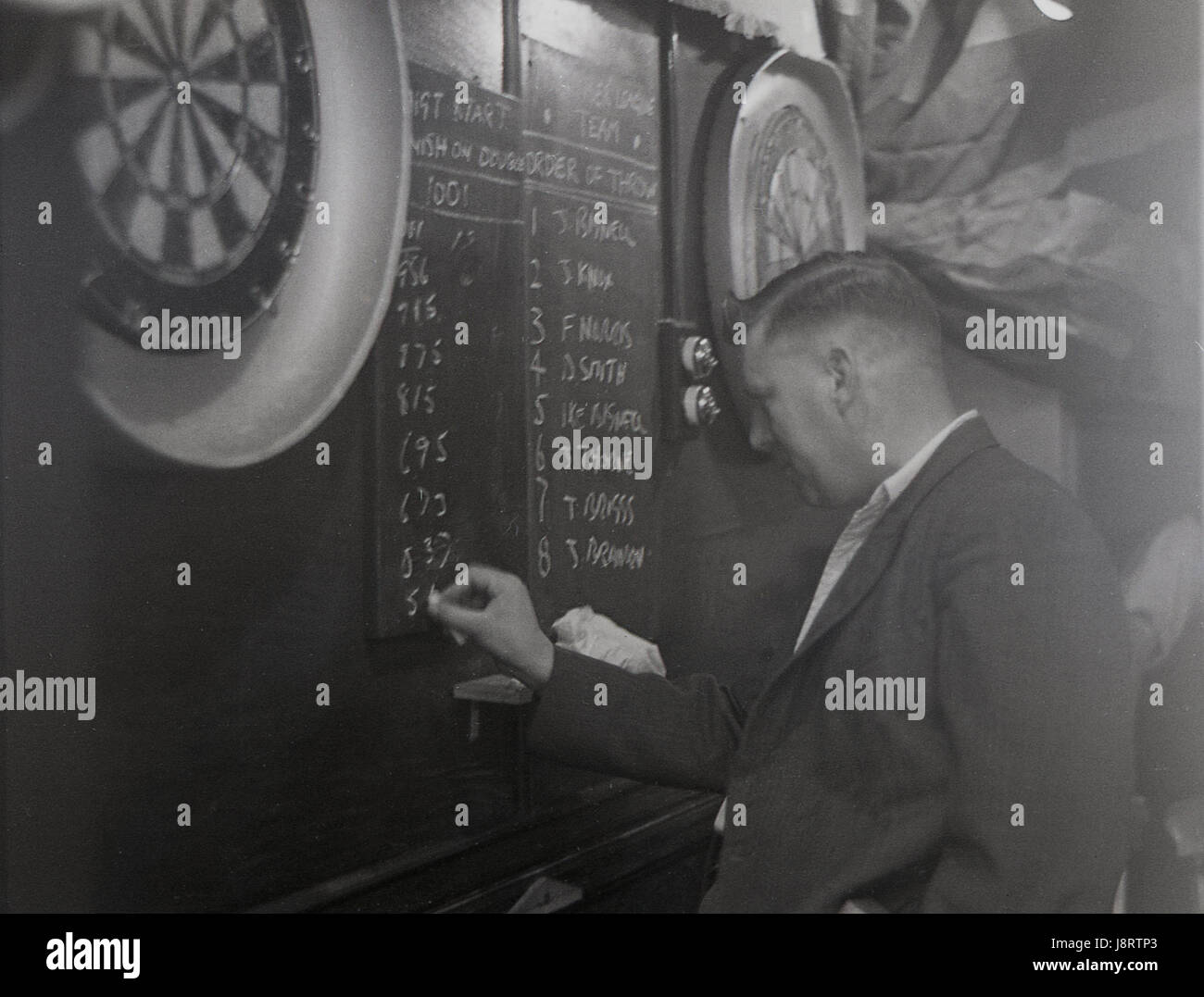 1950s, inside a hazy smoke fill pub, England, man chalks up the score during a darts match. Stock Photo