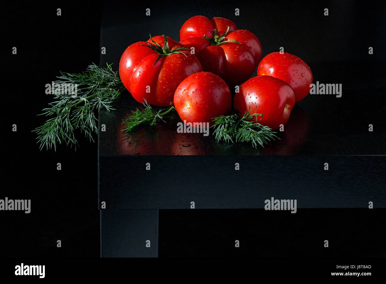 Three small . two large fresh tomatoes . sprig of dill and water droplets on a dark wooden background Stock Photo