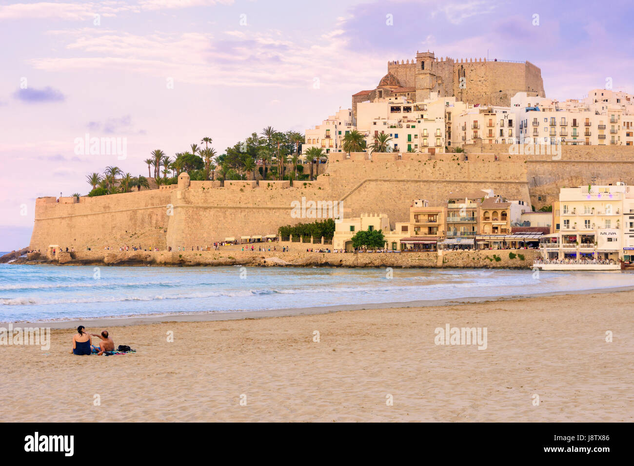 Papa Luna's Castle and old town overlooking a couple on Playa Norte beach at sunset, Peniscola, Spain Stock Photo