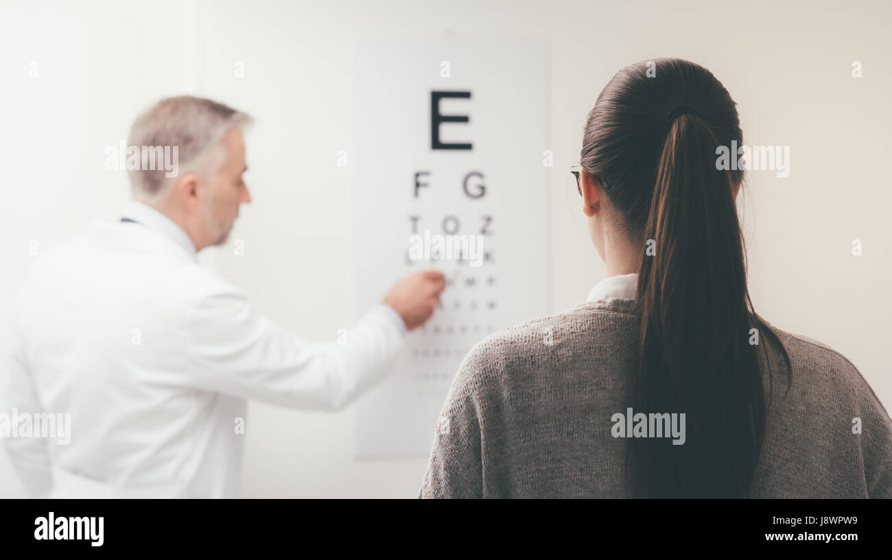 Woman reading the eye chart, the ophthalmologist is pointing at one letter and examing the patient, eye care concept Stock Photo