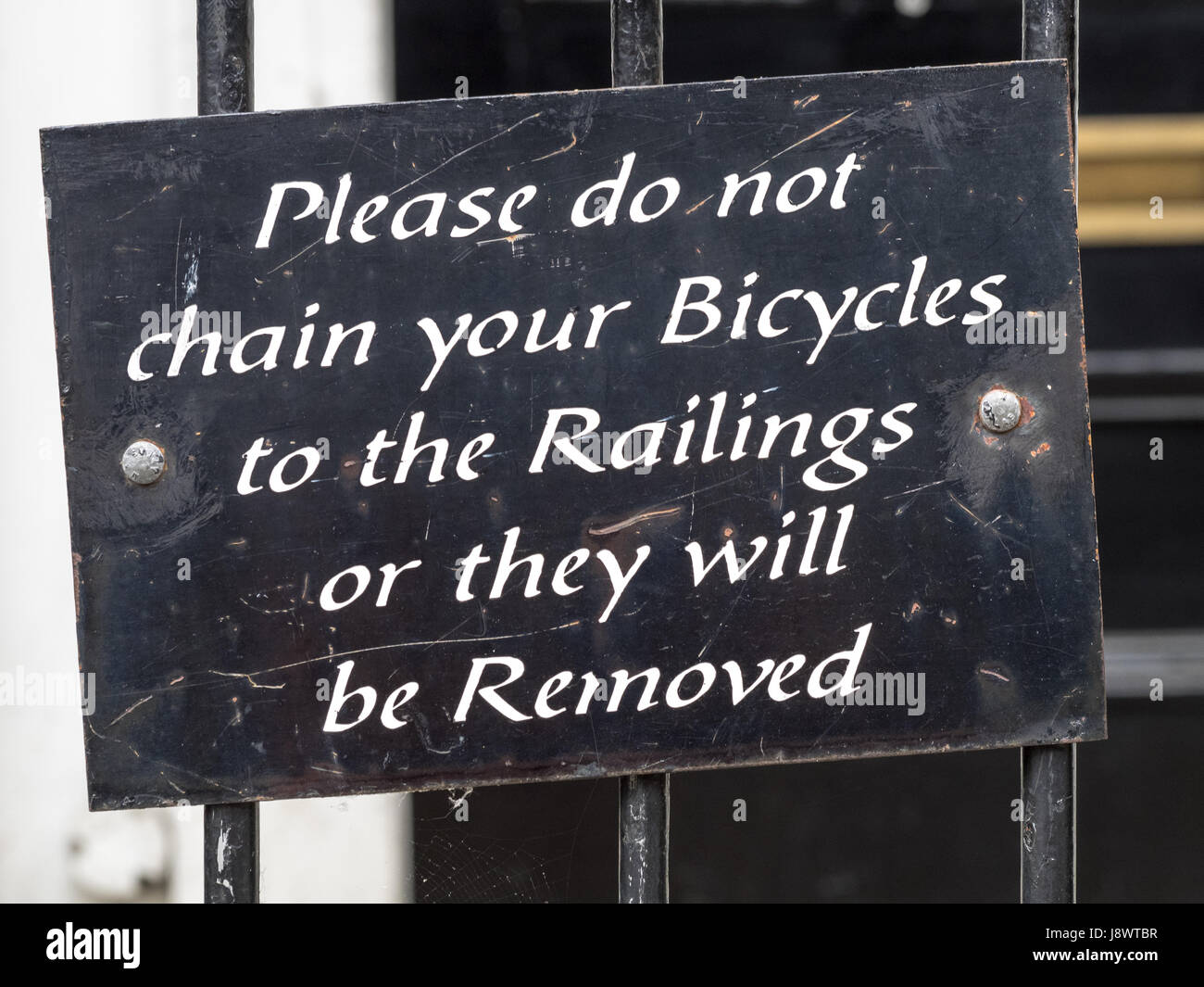 Lopsided sign asking not to chain bikes to the railings Stock Photo
