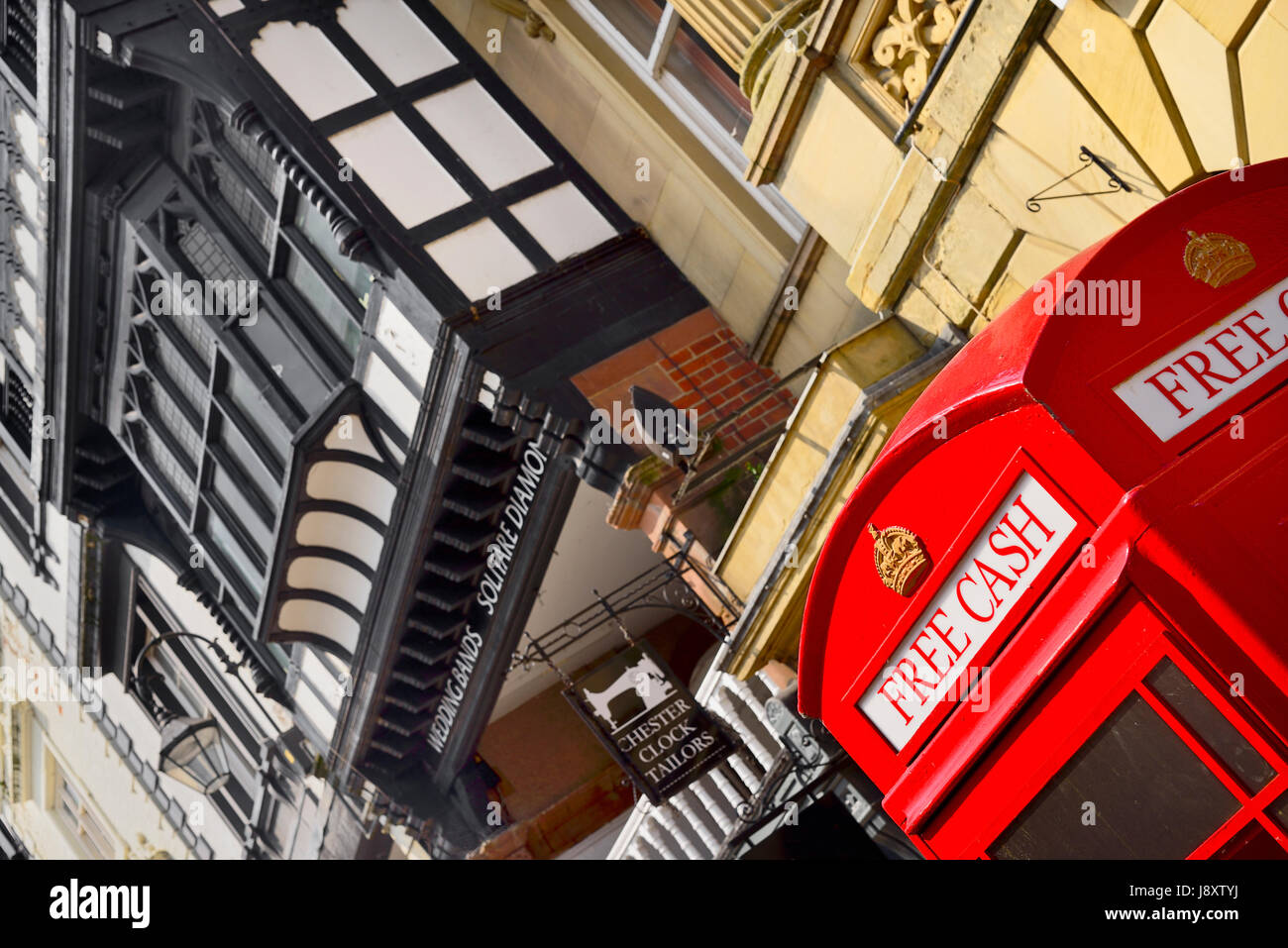 England, Cheshire, Chester, Iconic red telephone box converted to ATM on Eastgate Street with black and white architecture behind. Stock Photo