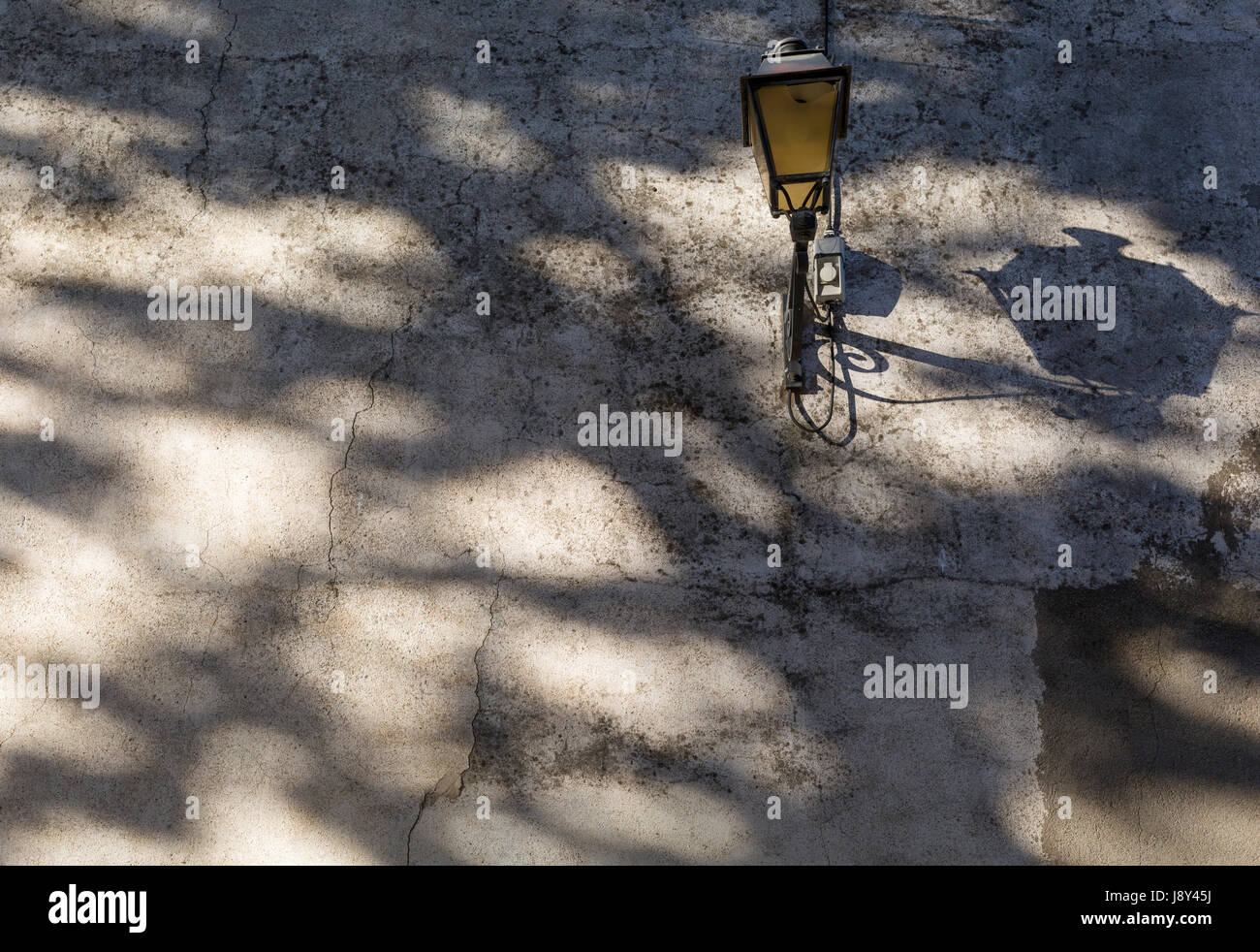 Shadow patterns and a street lamp on a wall on 25th May, 2017, in Lagrasse, Languedoc-Rousillon, south of France. Lagrasse is listed as one of France's most beautiful villages and lies on the famous Route 20 wine route in the Basses-Corbieres region dating to the 13th century. Stock Photo