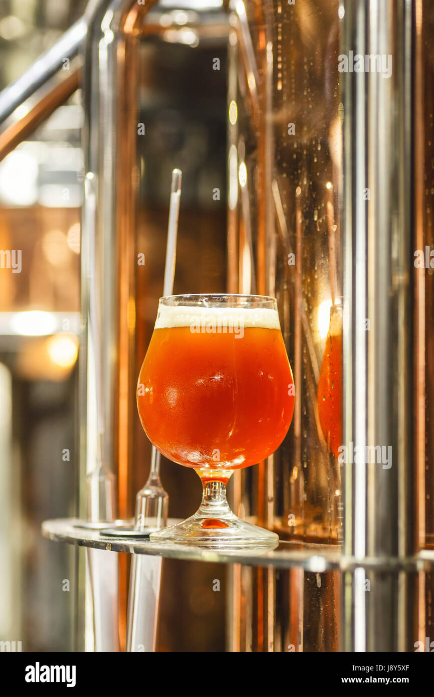 Glass full of amber ale beer standing near a working copper kettle in a commercial brewery with some measurement tools Stock Photo