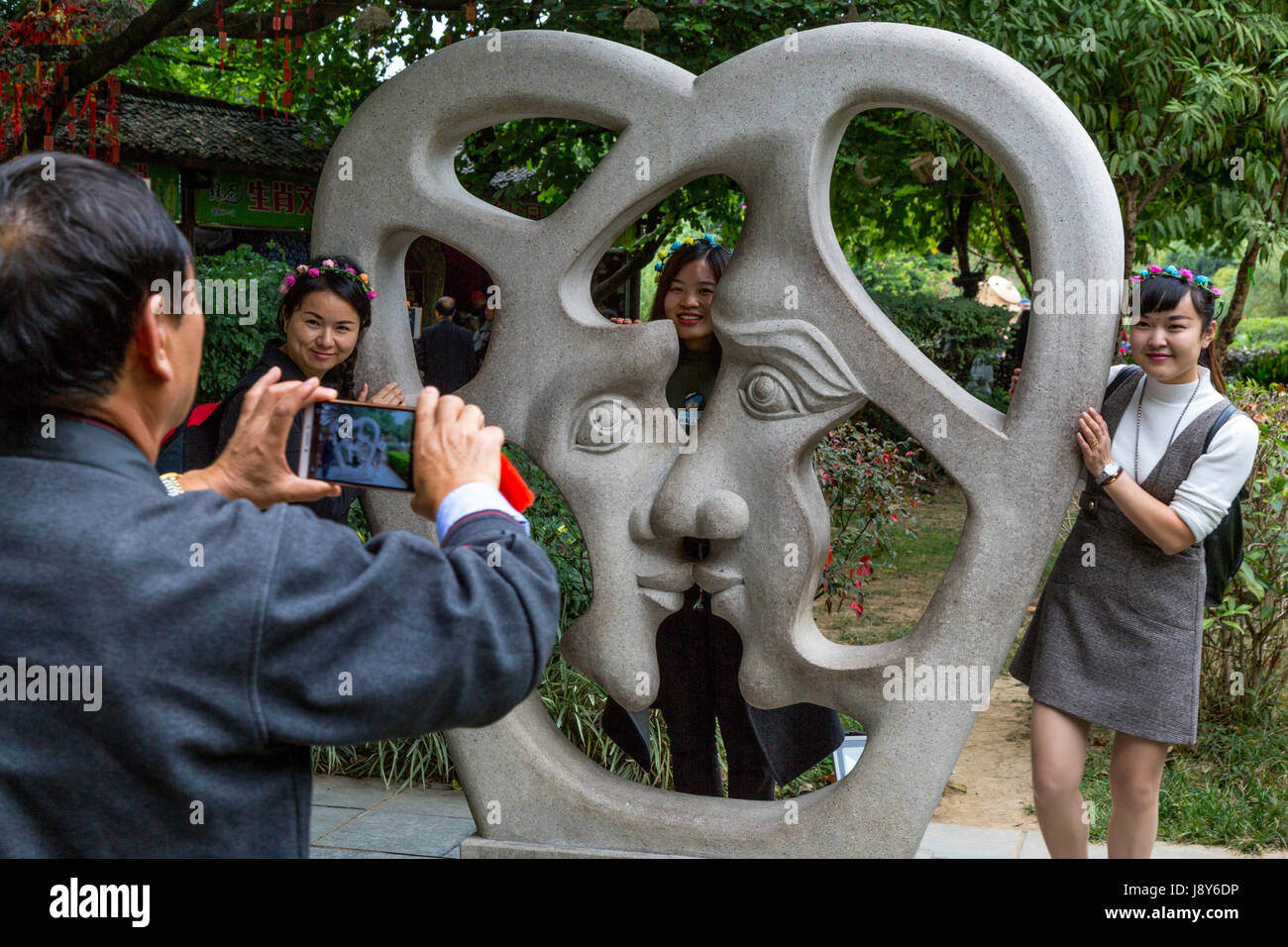 Guilin, China.  Elephant Trunk Hill Park.  Man Taking Picture of Three Women with Modern Sculpture Representing Love. Stock Photo