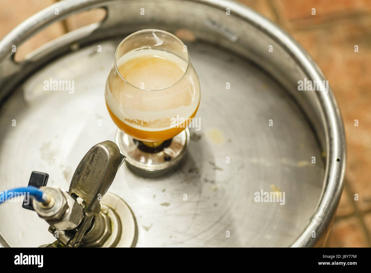 Glass of opaque wheat beer standing on a stainless steel keg at a brewery Stock Photo