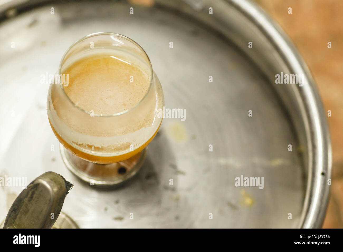 Glass of opaque wheat beer standing on a stainless steel keg at a brewery Stock Photo