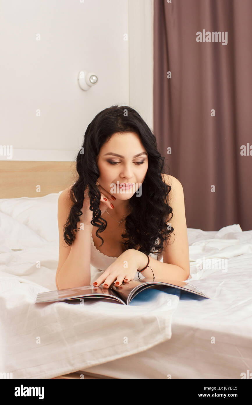Woman lying in bed while reading a magazine Stock Photo