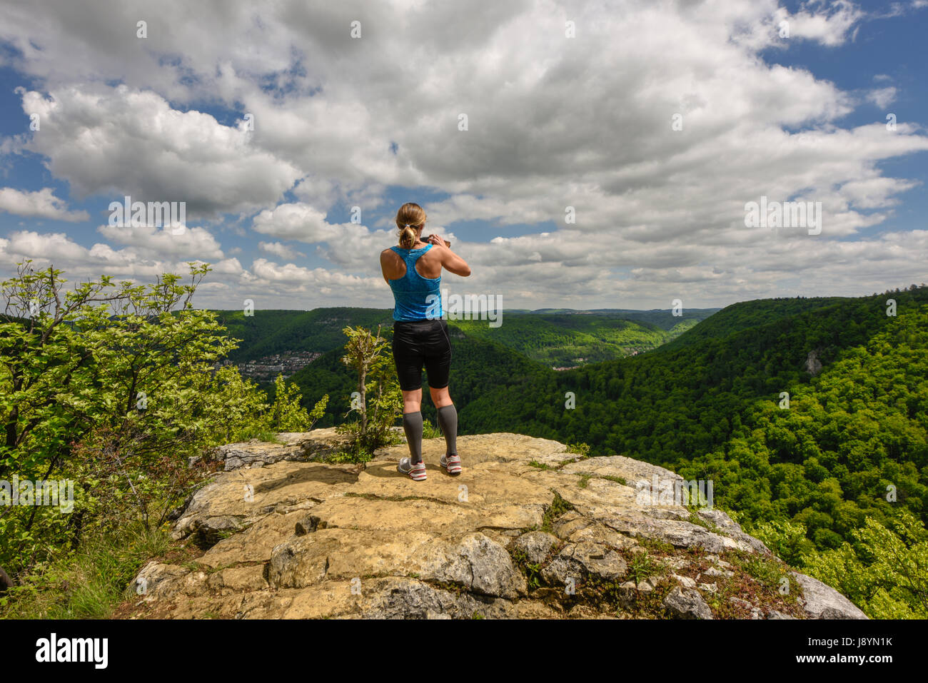 Sportive woman taking a photograph of a beautiful panorama. Taking a picture with mobile phone / smartphone / handy,  Bad Urach, Swabian Alps, Germany Stock Photo