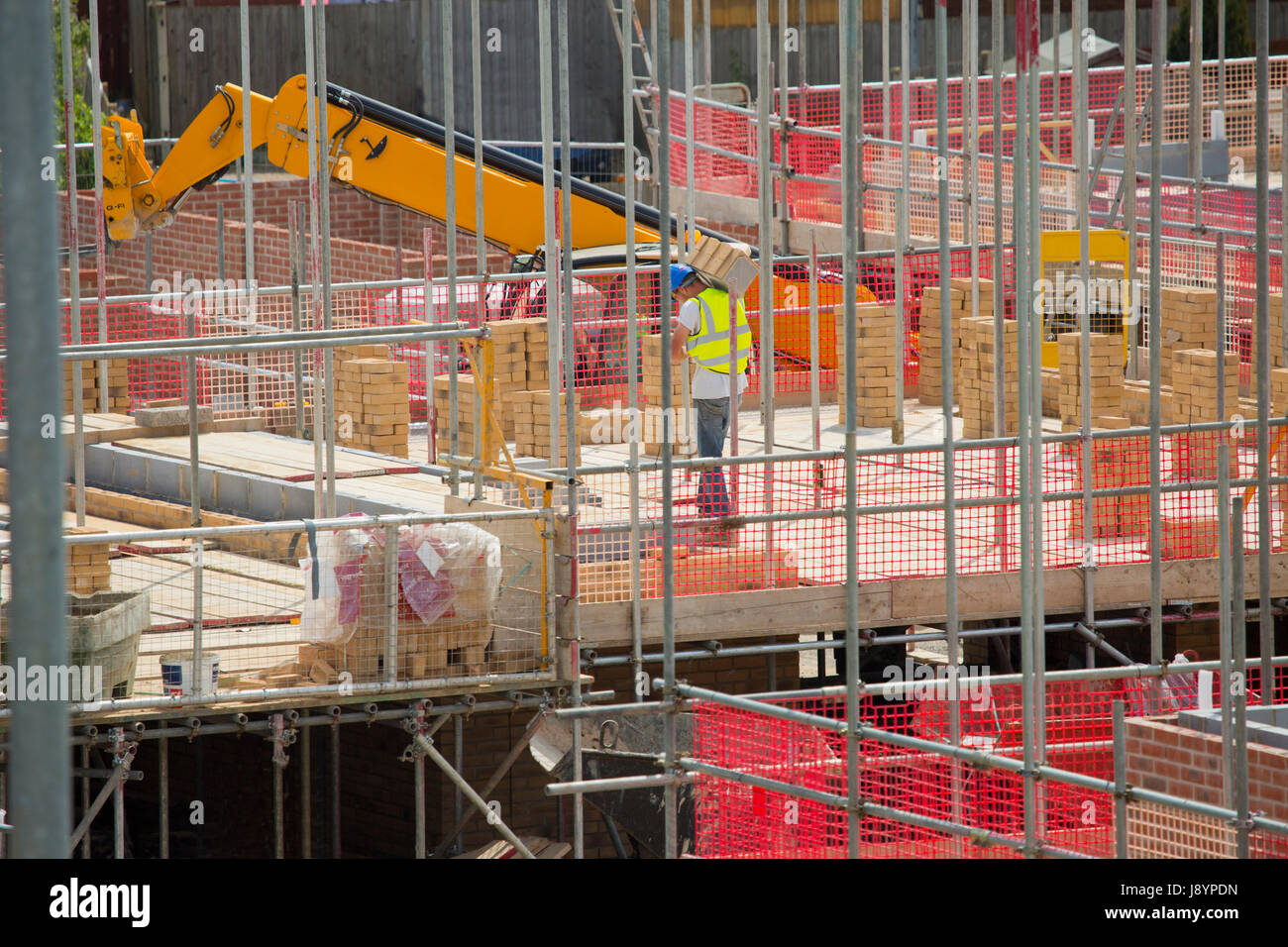A building site worker or hod carrier or labourer carrying bricks on a building site with scaffolding Stock Photo