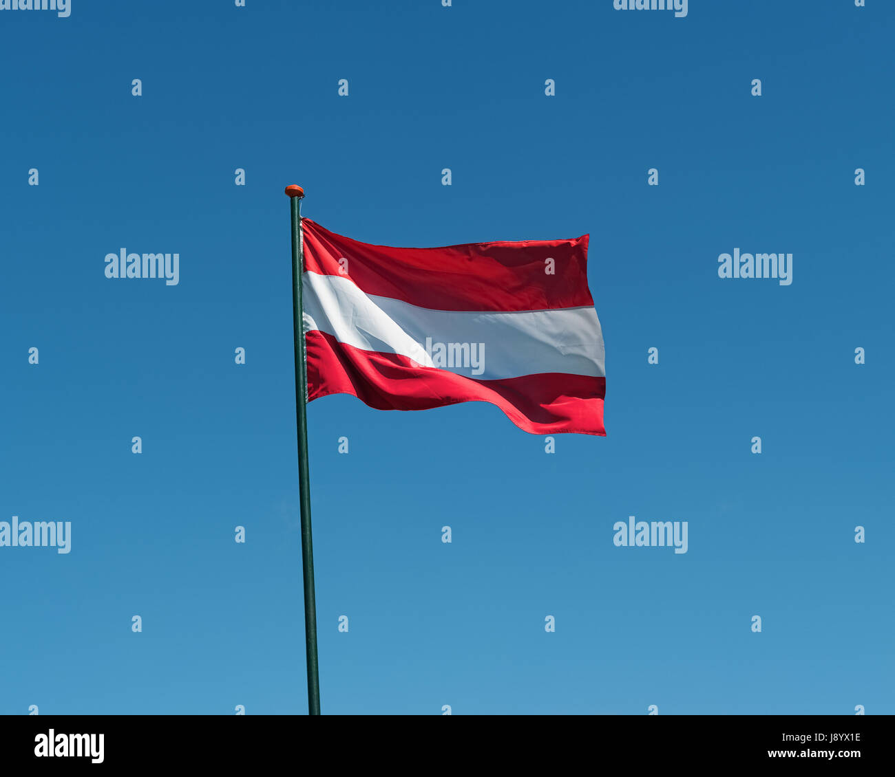 Flag of Austria on flagpole waving in the wind. Austrian national official flag on blue sky background. Patriotic symbol, banner Stock Photo