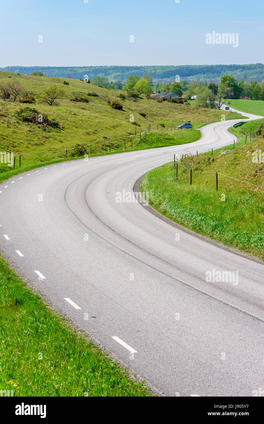 Curvy road through scenic landscape. Hills and meadows along the winding road. Location Brosarp in Scania, Sweden. Copy space on road. Stock Photo